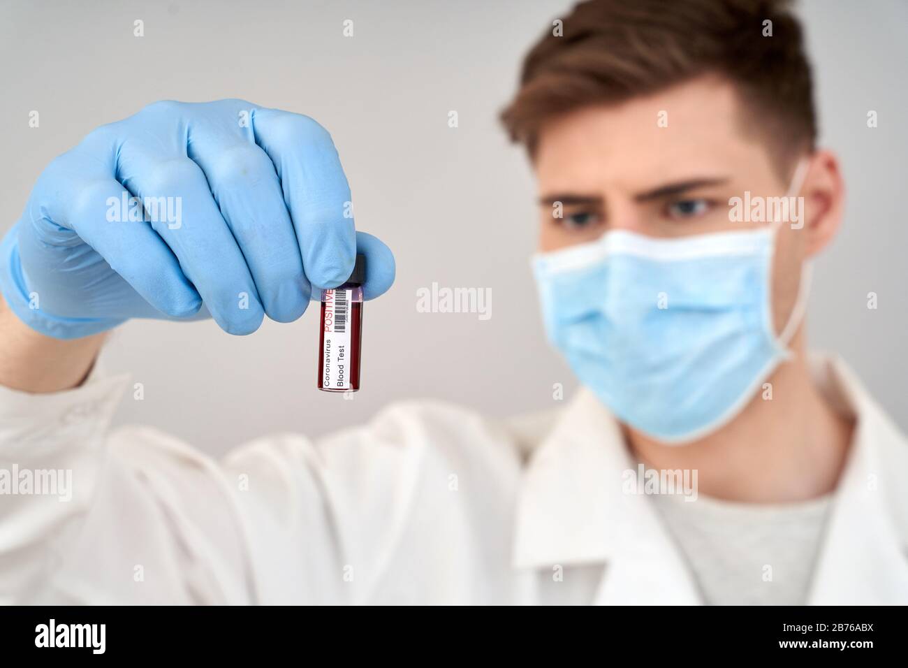 Man doctor wearing white robe and medical face mask standing isolated on gray backround holding virus in bulb close-up blurred pensive Stock Photo