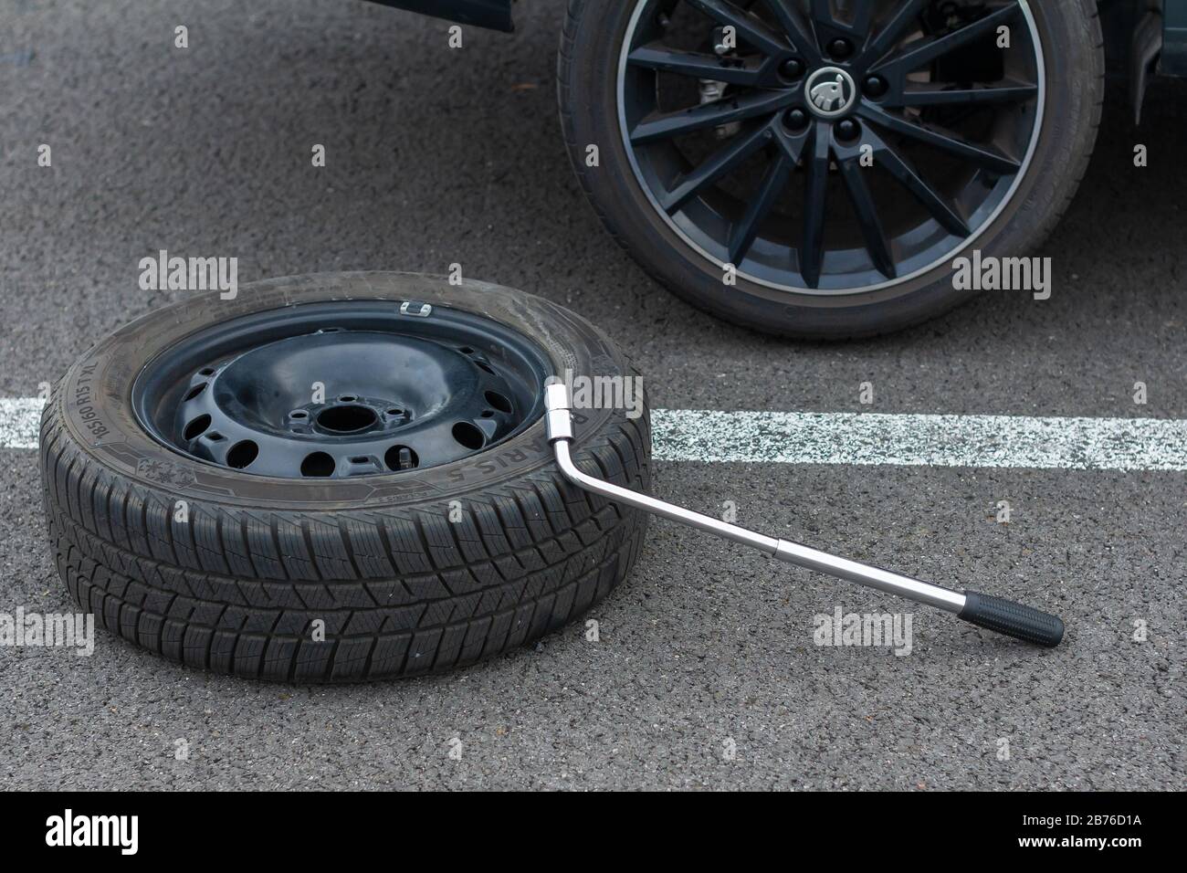 Top view on a flat tire car wheel and screwdriver are on a asphalt road on the broken car background. Jack is lifting up a vehicle. Automobile service Stock Photo