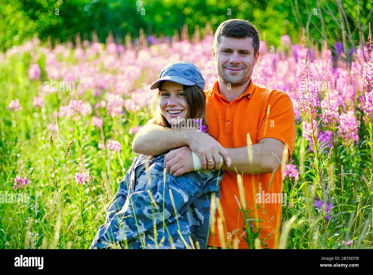 A young girl and a man are hugging each other in the tall grass with ...