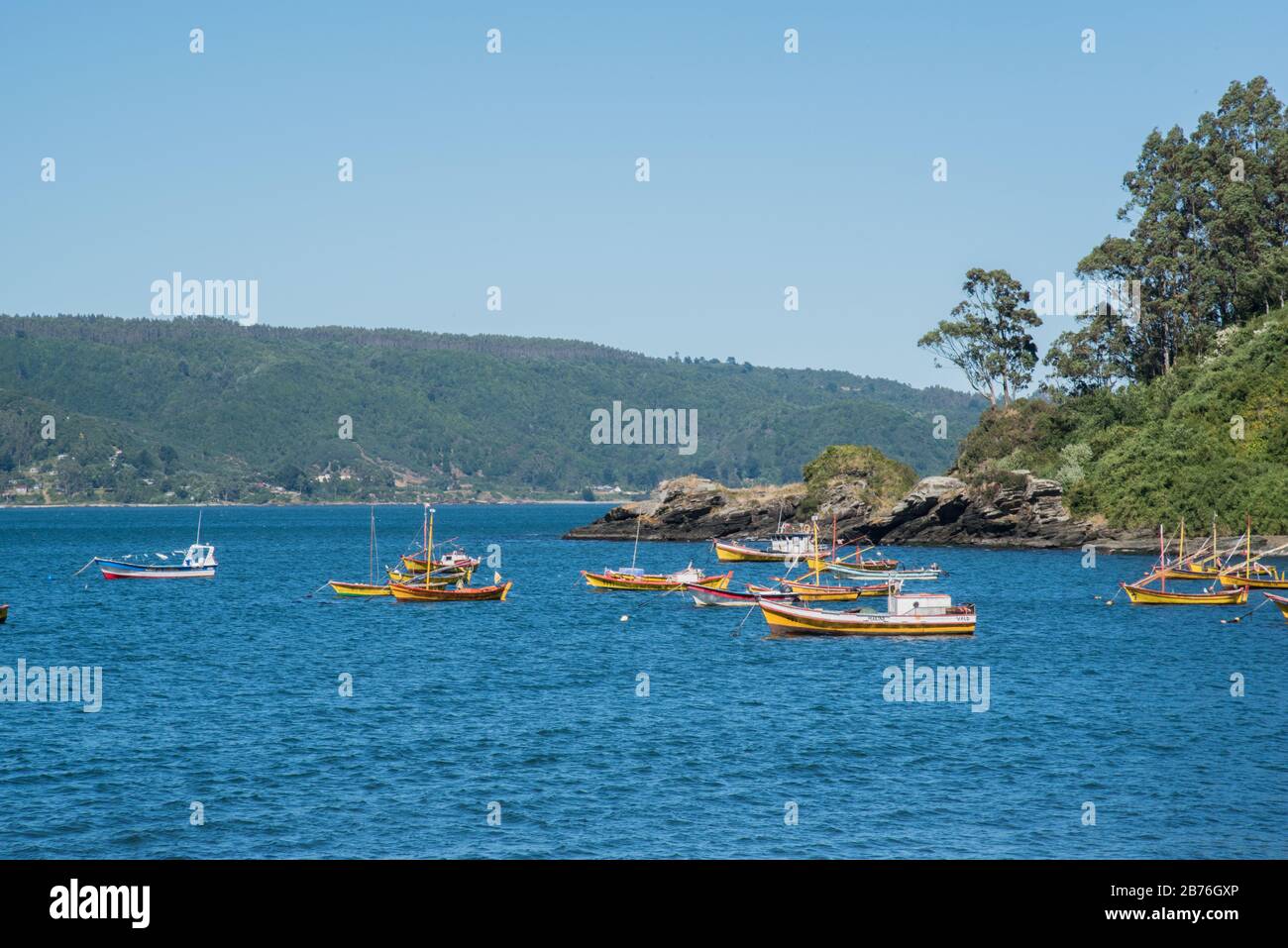 A cliff, Pacific Ocean and a mountain rangeon the back, and a bunch of fisher boats in Los Molinos, Valdivia, Chile Stock Photo
