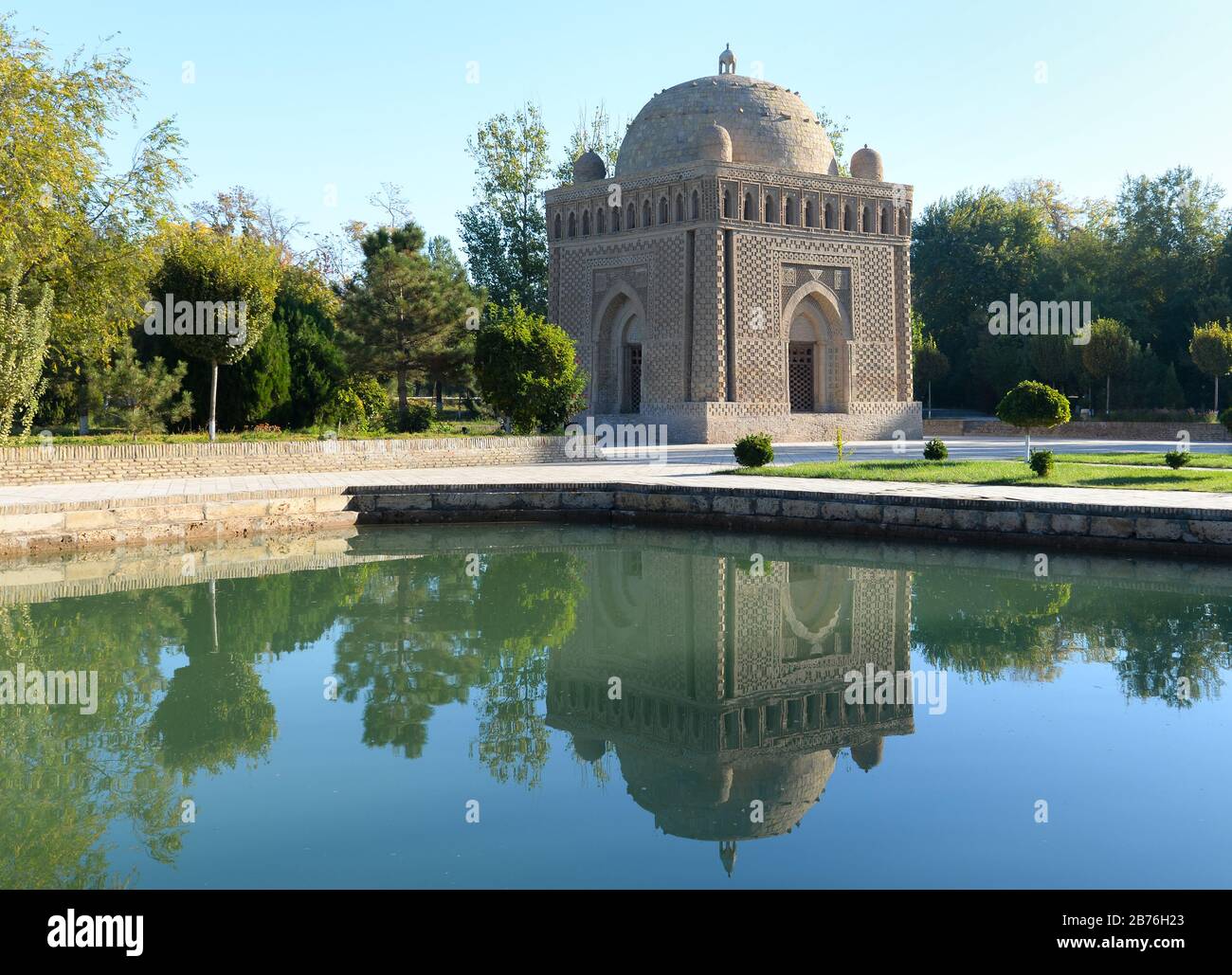 Samanid Mausoleum reflecting in the water in a park with vegetation in Bukhara, Uzbekistan. Iconic example of the early Islamic architecture in Asia. Stock Photo