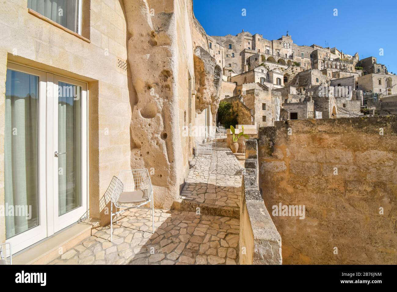 A modern sliding glass door and metal chair sit outside a patio in the ancient cave hillside city of Matera, Italy. Stock Photo