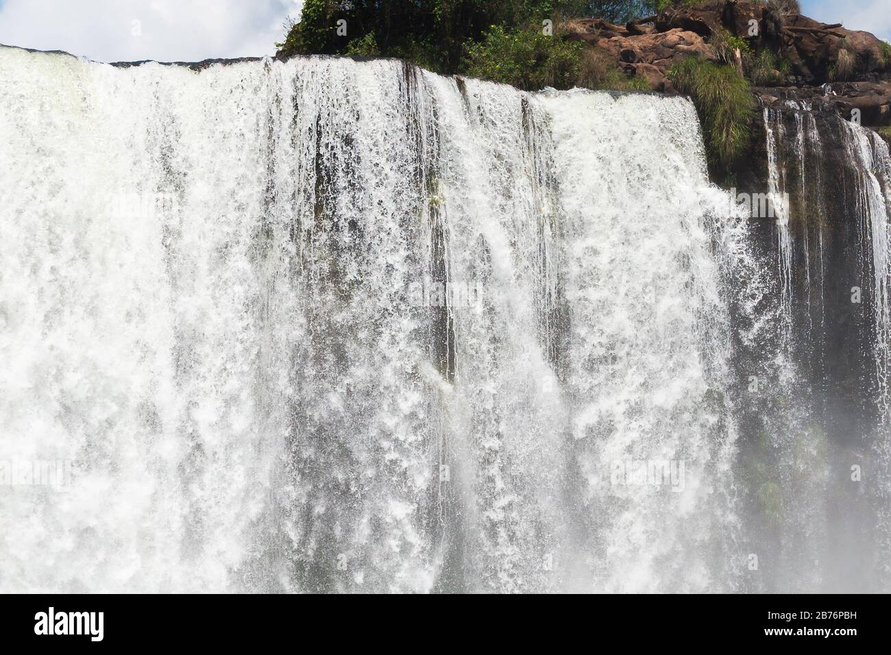 Close view of waterfall in high shutter speed photo with blue sky with a few clouds. Fall of Iguassu River located in Iguaçu National Park in Brazil. Stock Photo