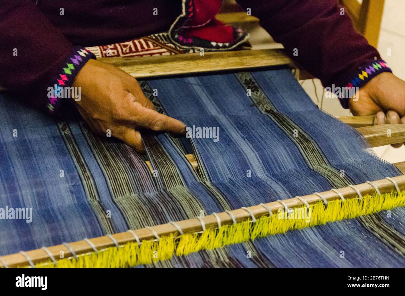 A Peruvian man weaves a loom inside of a workshop, Cusco, Peru Stock Photo