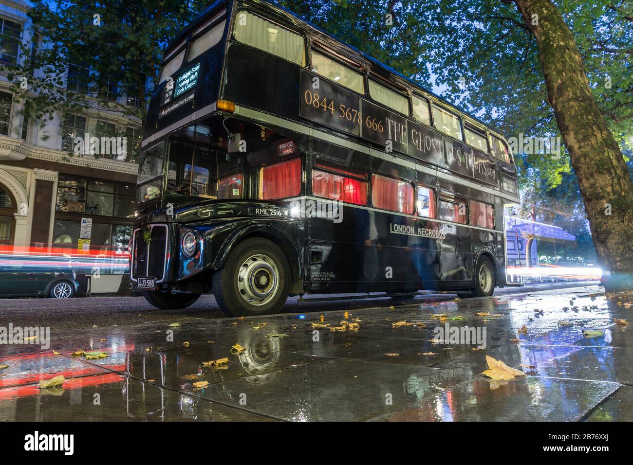 A black Routemaster double decker bus of The Ghost Tours company parked on a London street on a rainy evening Stock Photo