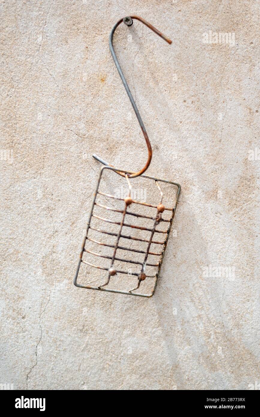 Rusted meat hook with a soap holder hanging on a screw on a concrete wall Stock Photo