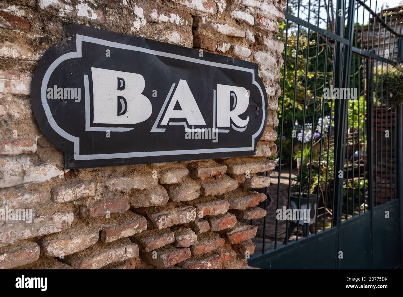 Poster 'bar' on a brick wall next to a green fence with a garden with flowers on the other side Stock Photo