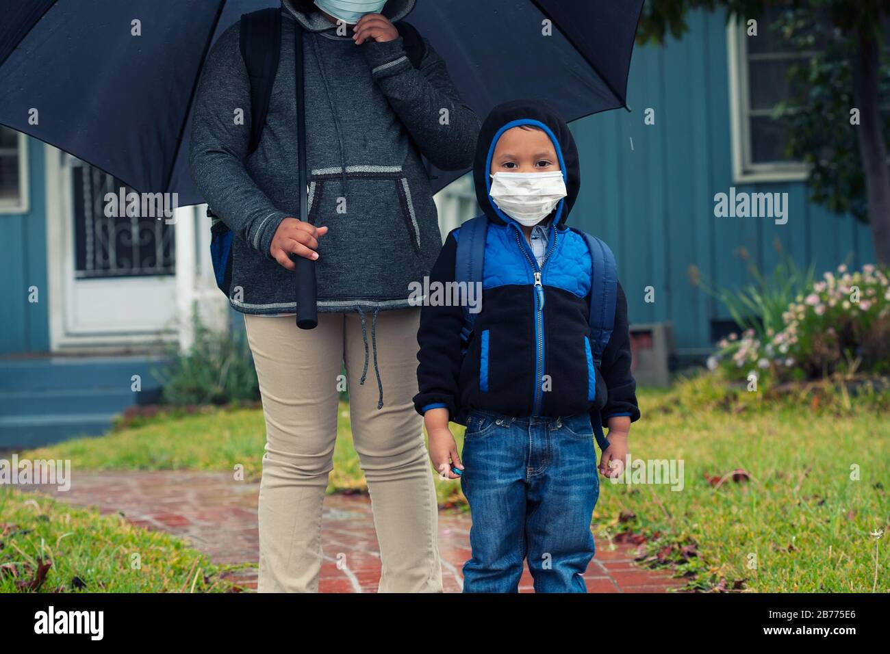 Little brother and older sister ready for school while wearing a face mask and backpacks during virus outbreak. Stock Photo