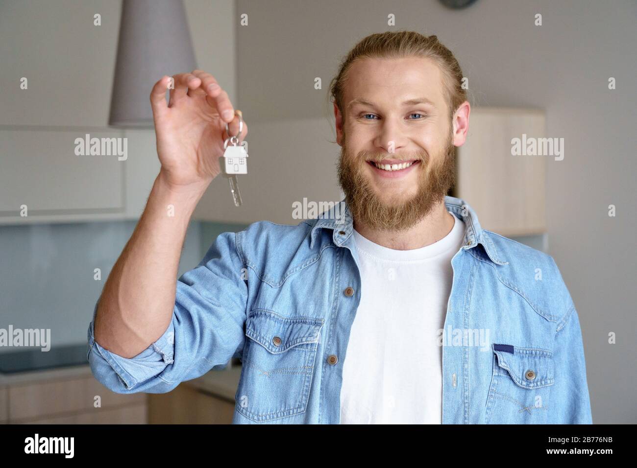 Young man hold keys modern flat smile background real estate concept copy space. Stock Photo