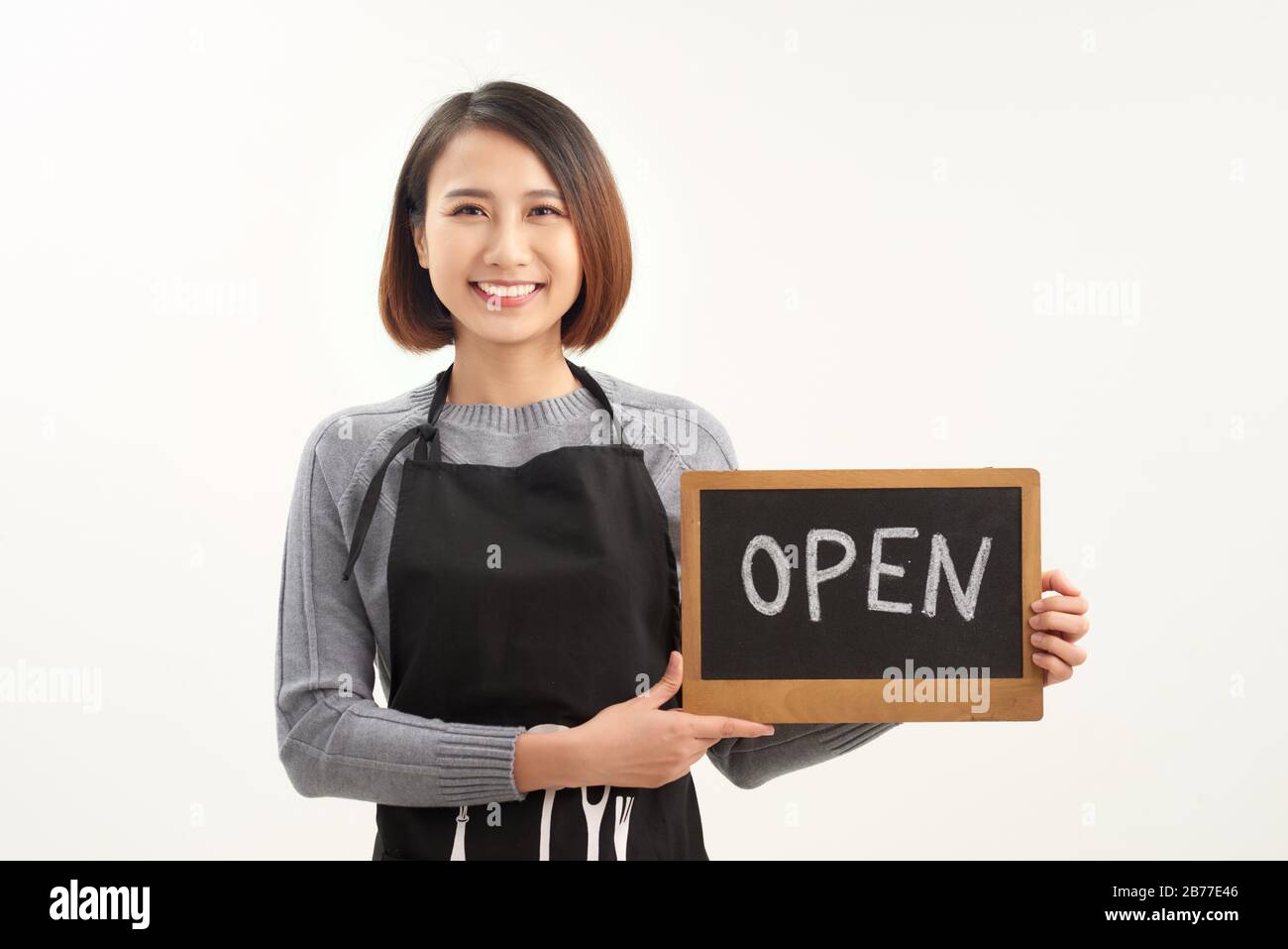 It's open here. A smiling woman is holding a sign with the inscription 'open' on a white background isolated. Stock Photo