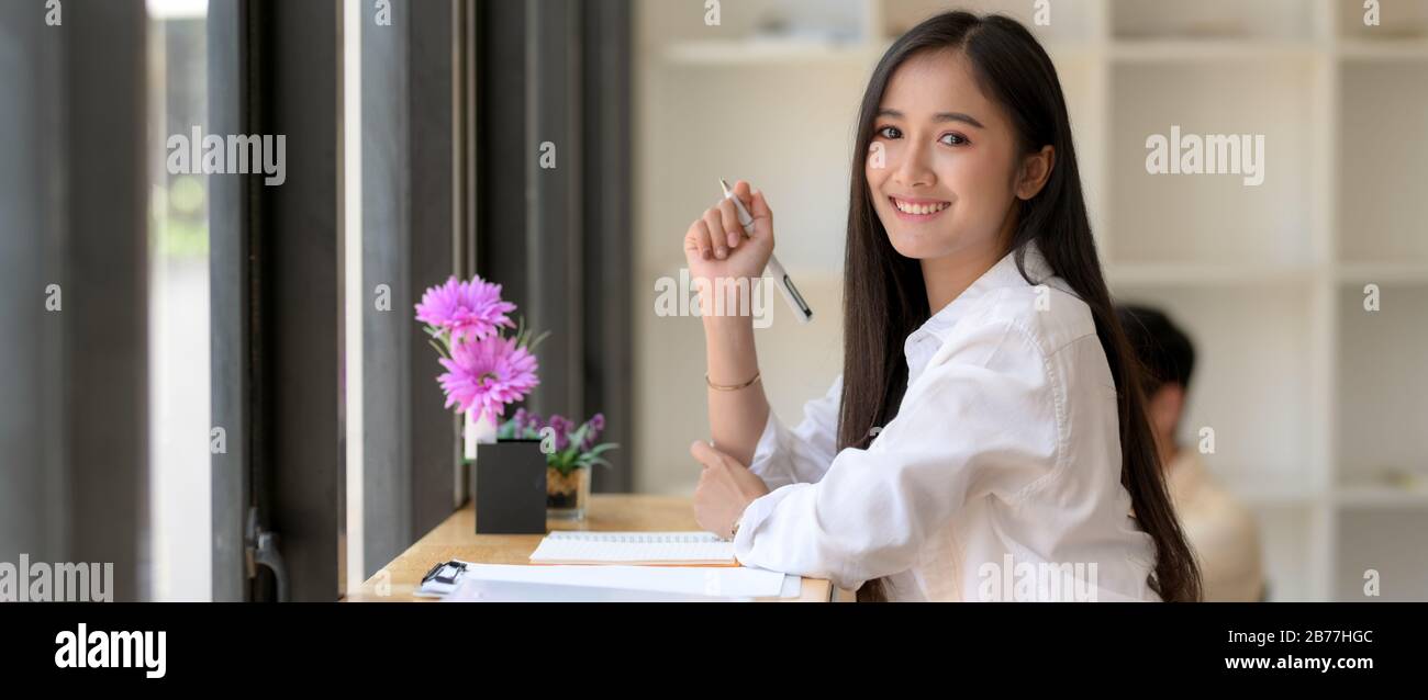 Side view of happy female university student preparing for her exam while sitting on wooden stool bar in cafe Stock Photo