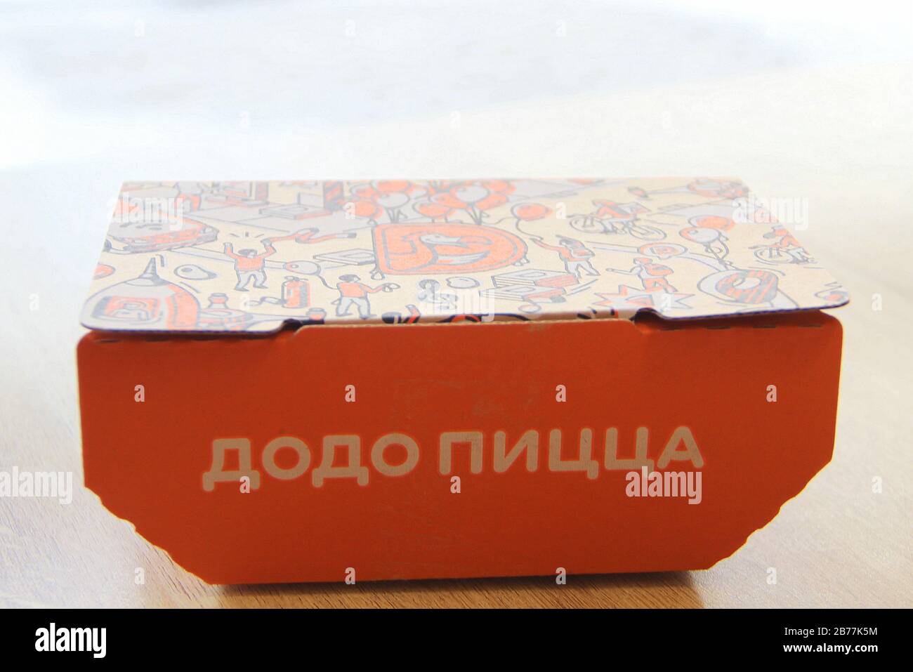 08-02-2020, Russia, Syktyvkar. Orange cardboard company box for Dodo snacks with a side inscription pizza and a corporate design and logo on the lid is standing on a table in a restaurant near the window. Stock Photo