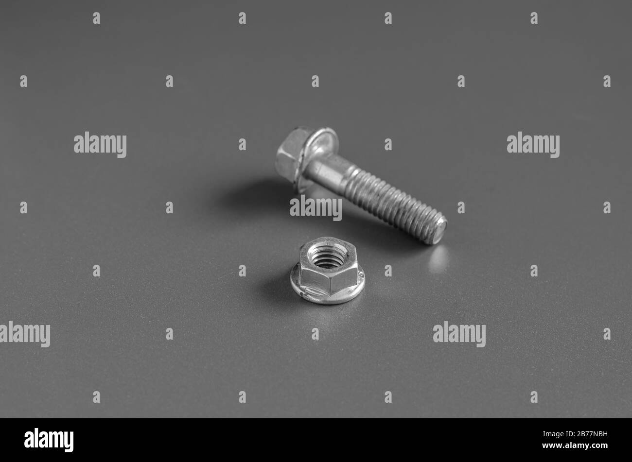 Bolt and nut on a gray background. Close-up nut with skirt and used bolt. Eye level shooting. Selective focus. Landscape photo arrangement. Stock Photo