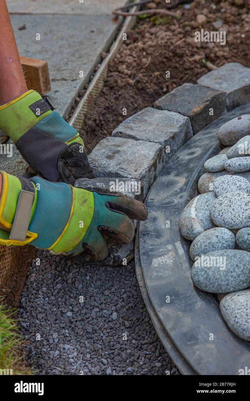 hands with work gloves arranging gritting material and basalt cobblestones into the curb of a garden fountain Stock Photo