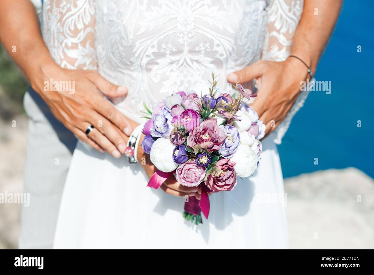 Purple bouquet of artificial roses in the hands of the bride in a white dress. Stock Photo