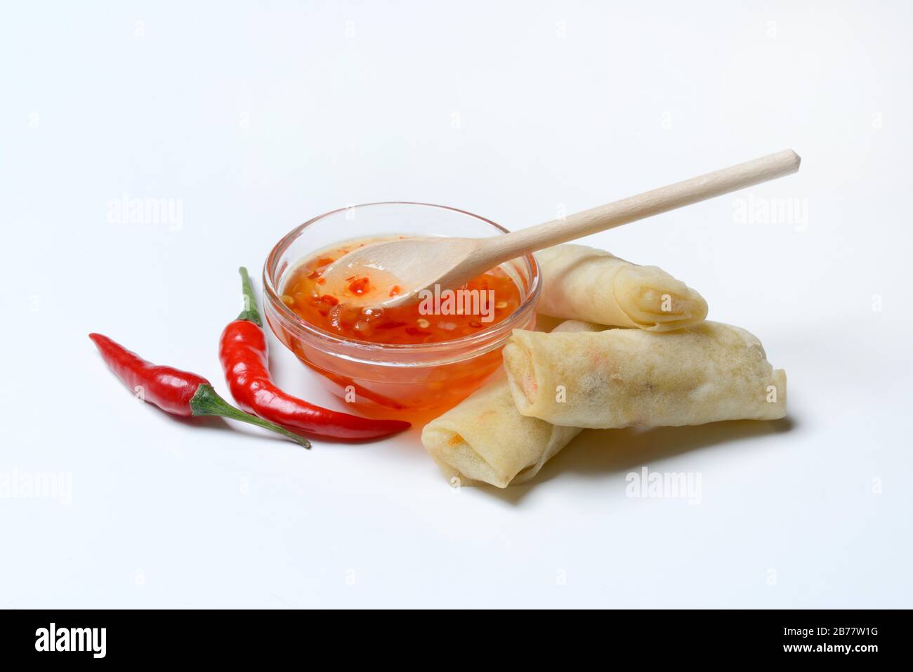 Chilli sauce in small bowls with chilli peppers and mini spring rolls