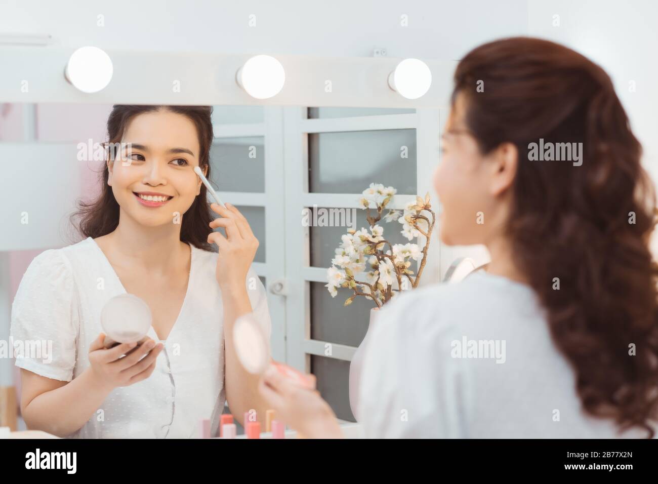 Young lady with pocket mirror using soft brush to smear eyeshadow Stock Photo