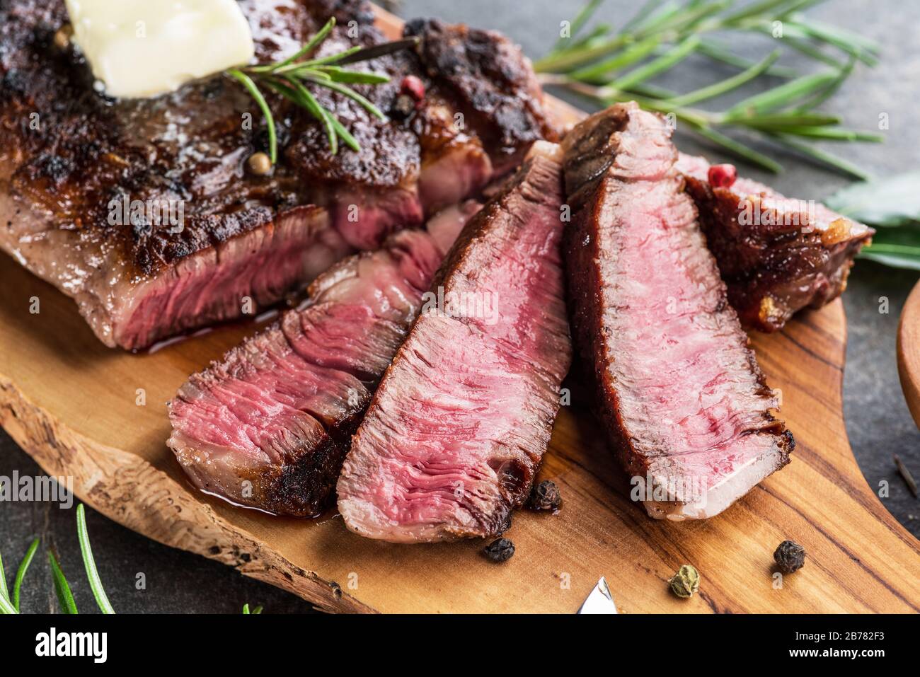 Medium rare Ribeye steak with herbs and a piece of butter on the wooden tray. Stock Photo