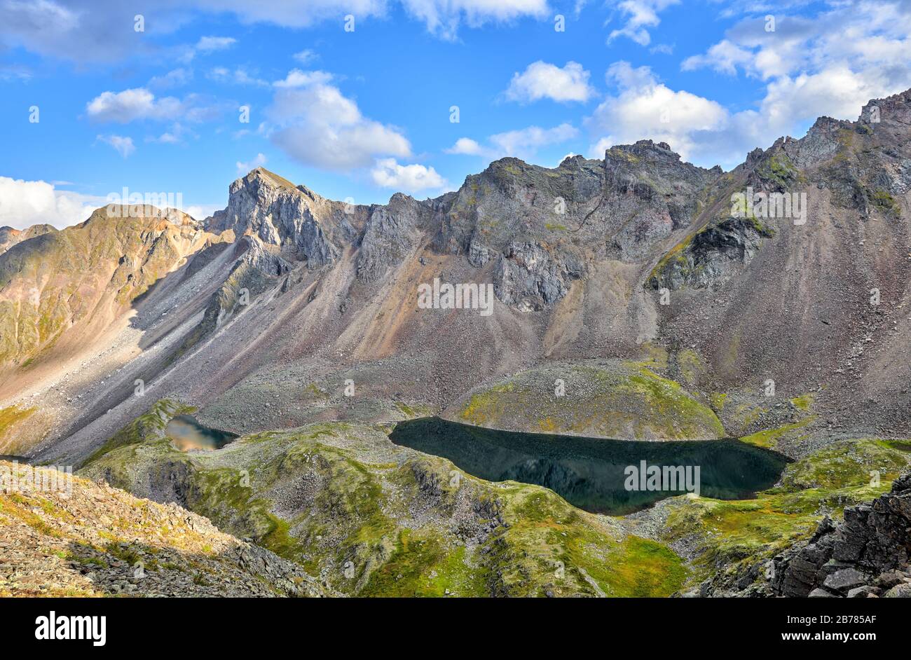 Deep dark lake in a hanging valley under a mountain range. Several lakes are located steps down. Eastern Sayan. Russia Stock Photo