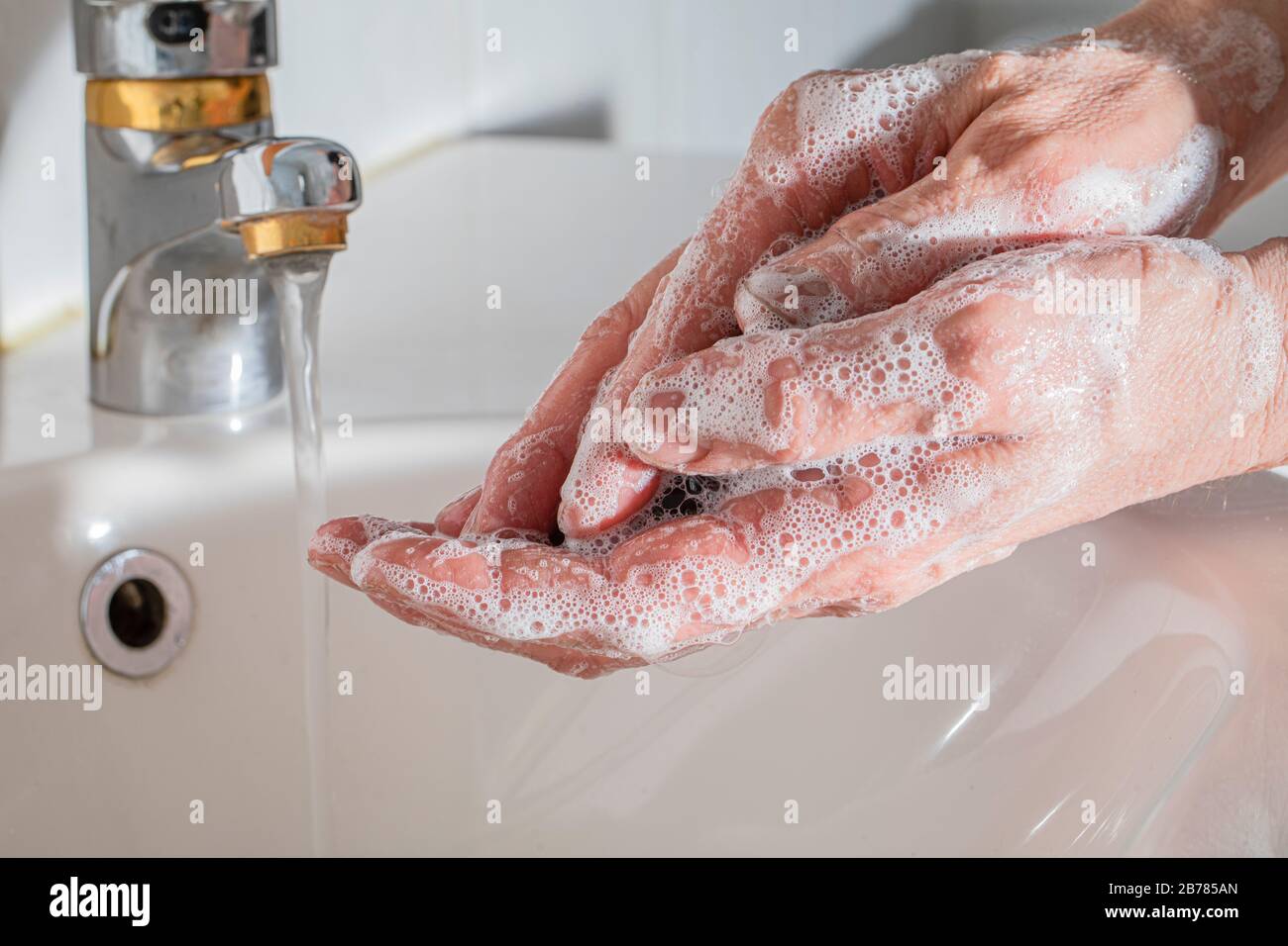 Male hands being washed hands in the bathroom, The hands are frothy of soap. and there is a running faucet in the background.  Corona virus covid 19 s Stock Photo
