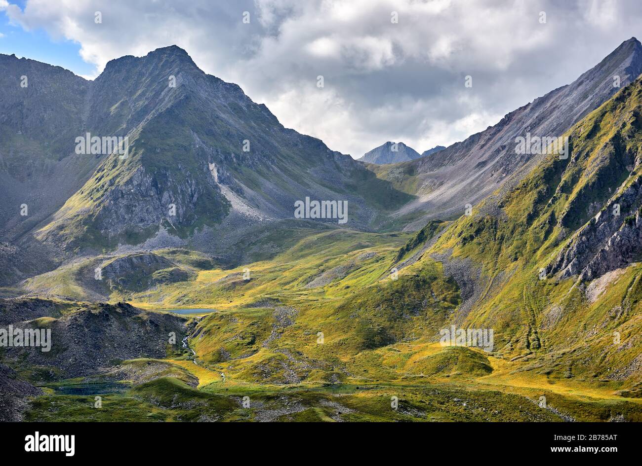 Alpine tundra and lakes at head of Siberian river. The upper part of the mountain valley is of glacial origin. Sunlight illuminates selected areas of Stock Photo