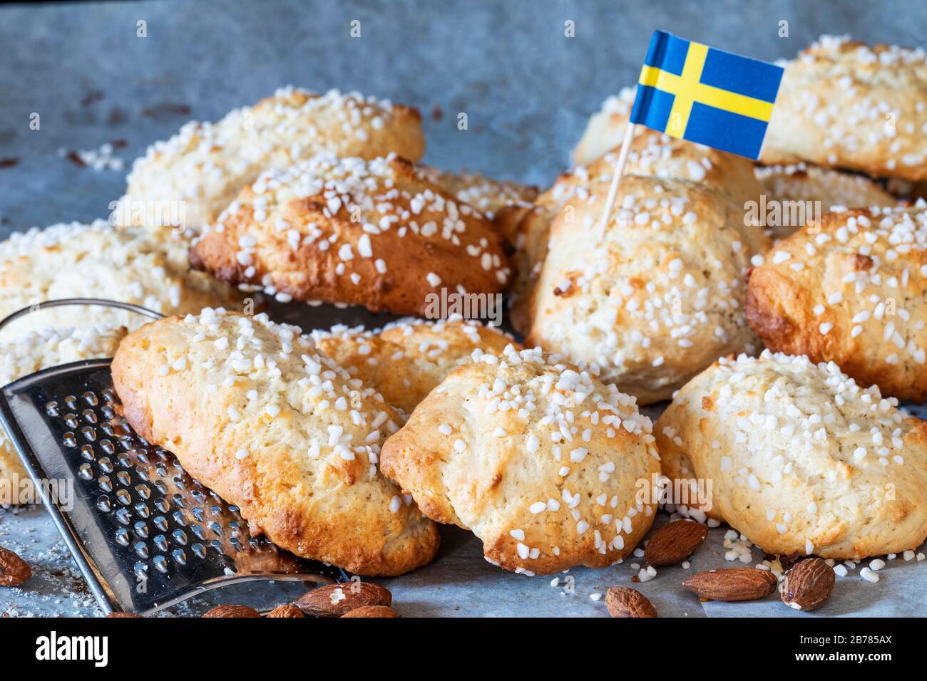 Swedish fika, swedish soft almond cookies mandelkubb with a swedish flag. There is a grater and almonds ascattered around the buns. Stock Photo