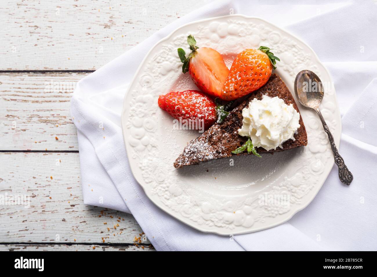 A slice of sticky chocolate mud cake, brownie or traditional Swedish kladdkaka on a white wooden table with a white napkin in the background. The cake Stock Photo