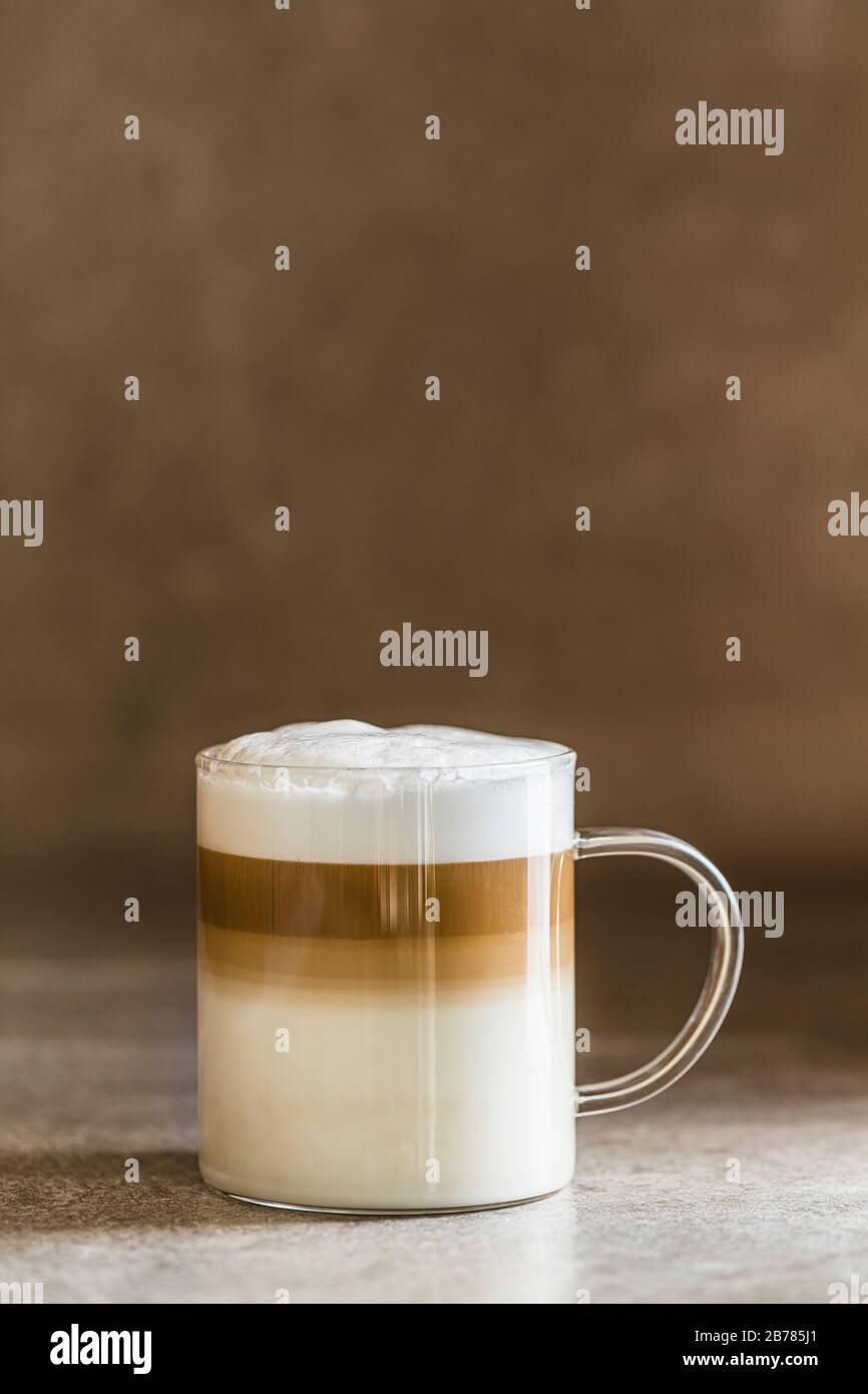Caffe latte macchiato coffee on a brown gray table with beige background. Copy space room for text at the top. Stock Photo