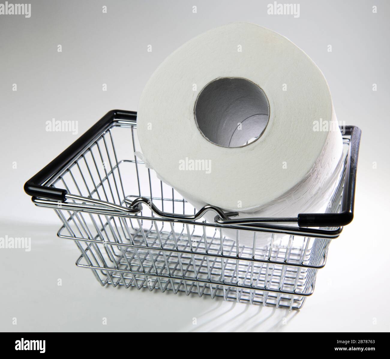 Supermarket shopping basket with giant toilet roll on a white background, backlit Stock Photo