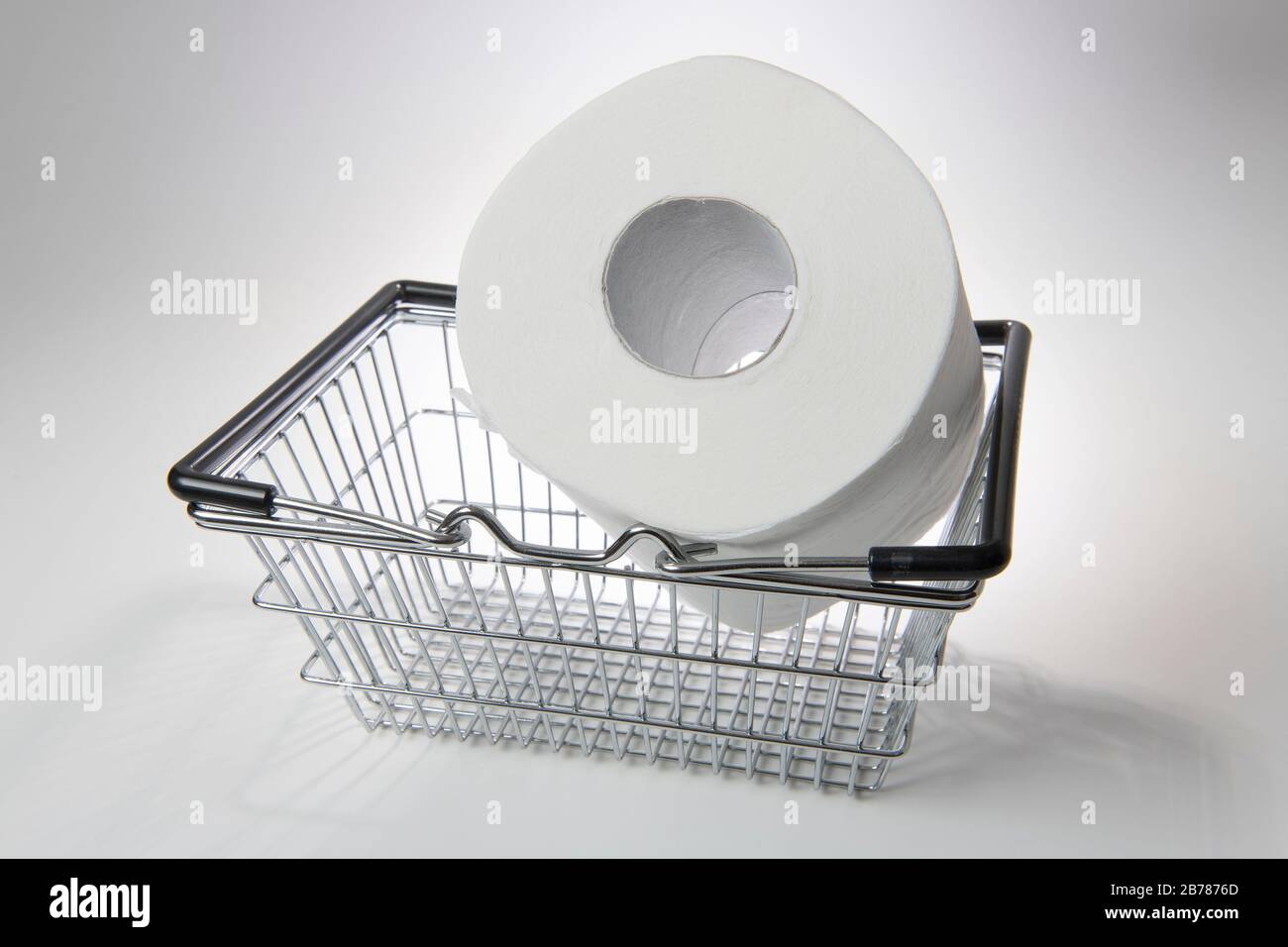 Supermarket shopping basket with giant toilet roll on a white background, backlit Stock Photo