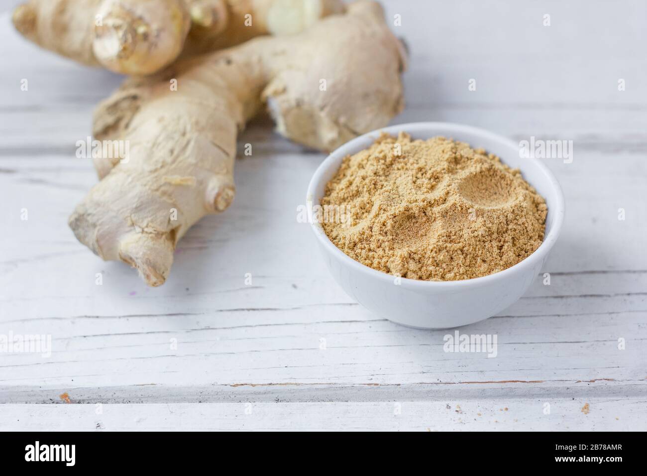 Grounded ginger and ginger root on white wooden surface. Stock Photo