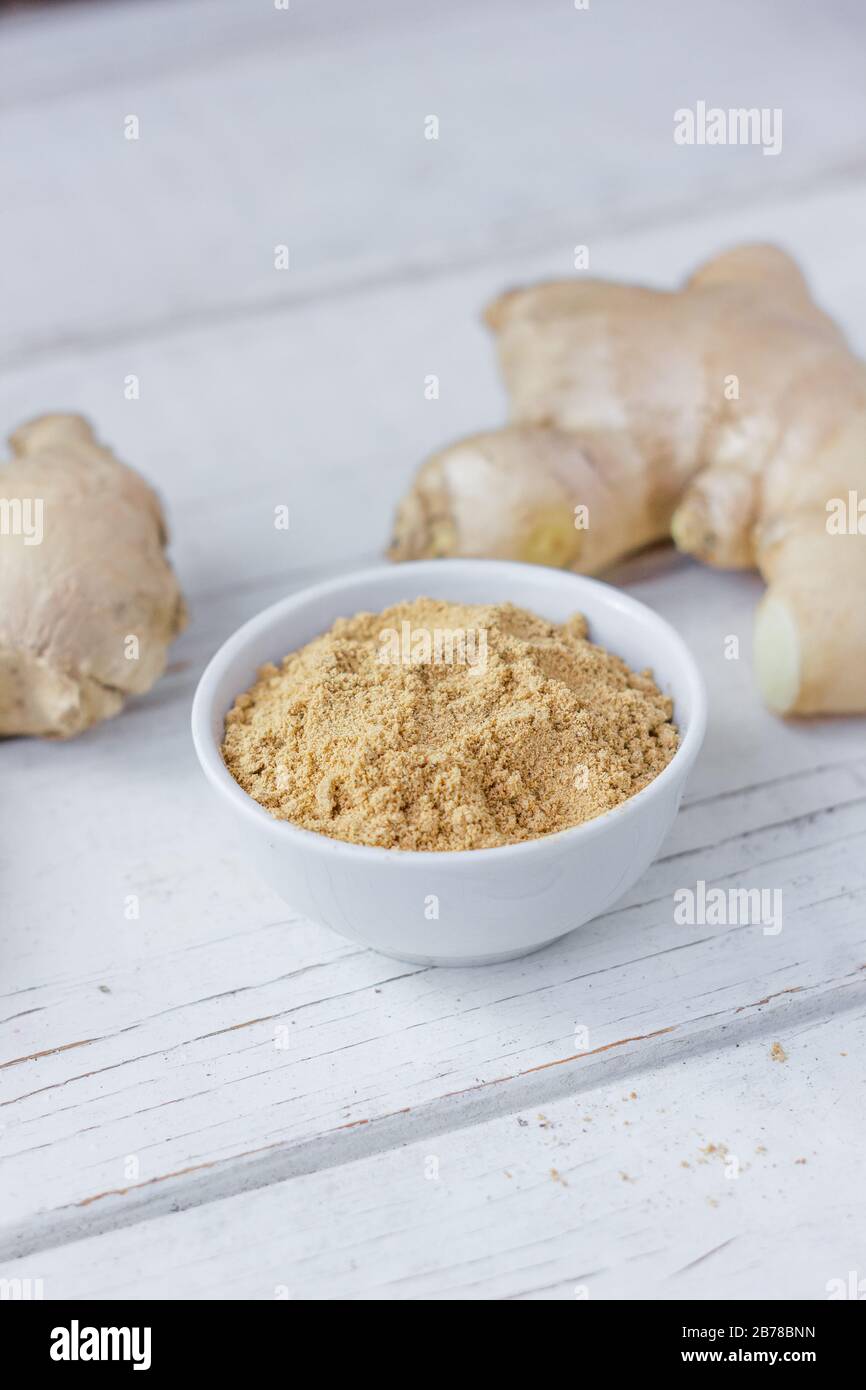 Grounded ginger and ginger root on white wooden surface. Stock Photo