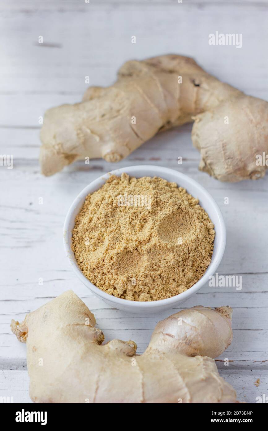 Grounded ginger and ginger root on white wooden surface. Stock Photo
