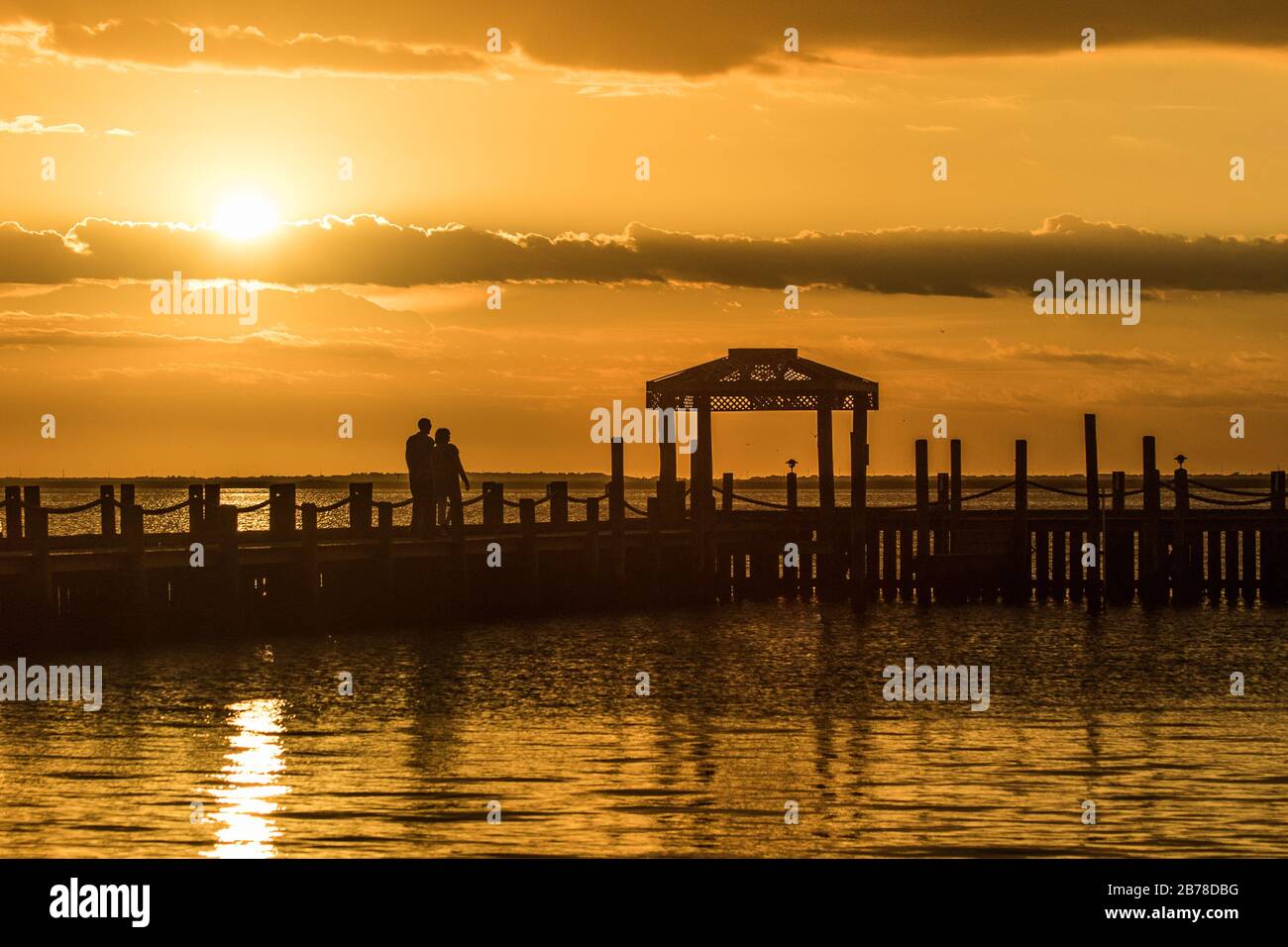 A couple watches a yellow sunset over Brnegat Bay from Long Beach Island at the Jersey shore Stock Photo