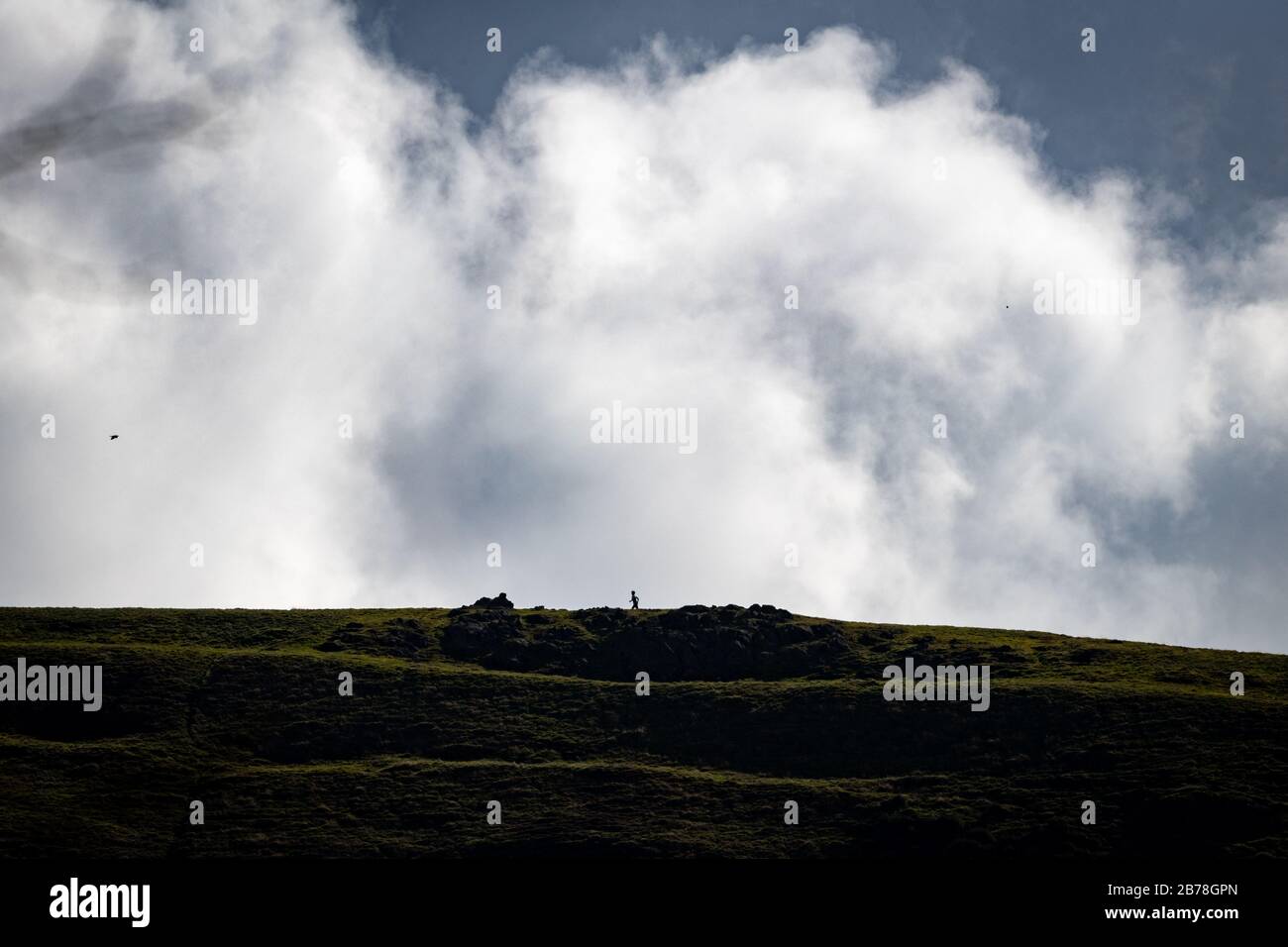 Long distant shot of a runner on the distant Earl's Hill in Shropshire shot against billowing white clouds. Runner running along the horizon. Stock Photo