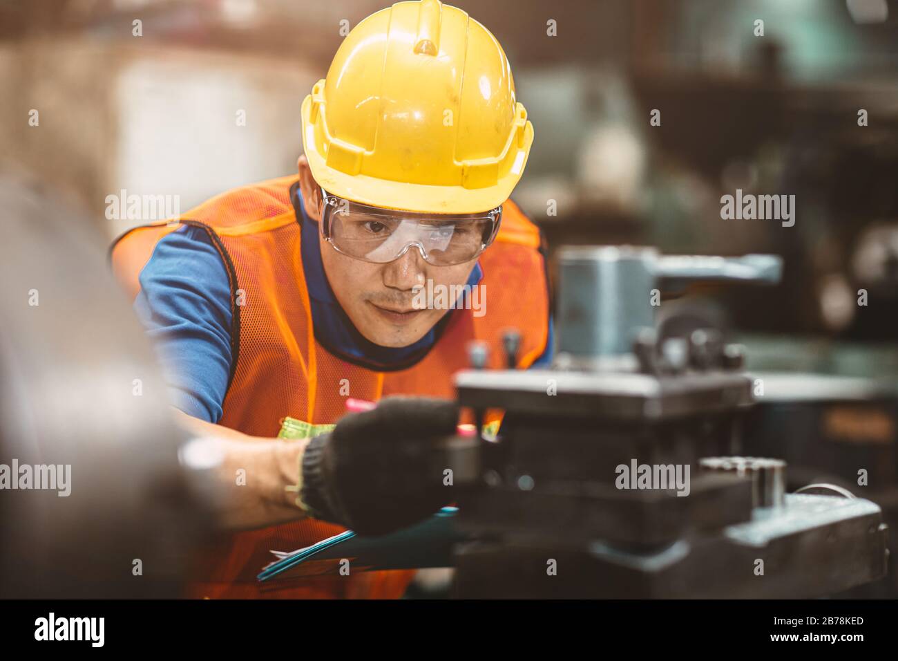 Asian Chinese engineer worker wearing safety suit helmet and eyes protection glasses focus at work inspection and checking production process on facto Stock Photo