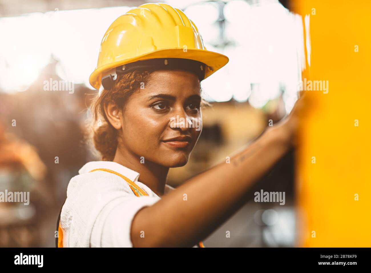 happy African American woman worker with safety suit helmet enjoy smiling working as labor in heavy industry factory with steel machine operator for g Stock Photo