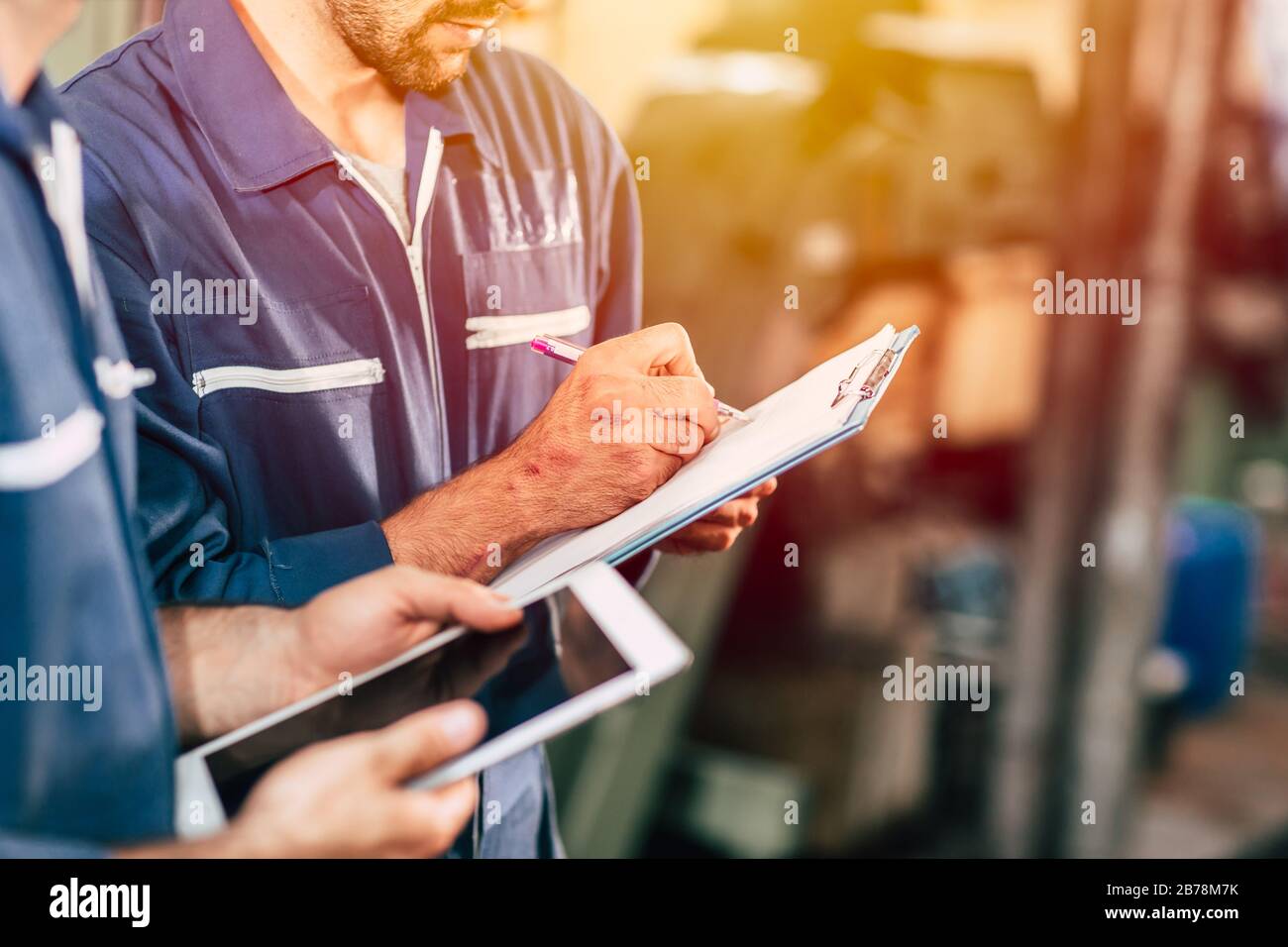 worker taking note using pen and paper with new young engineer using computer tablet for work faster and more efficiency. Stock Photo