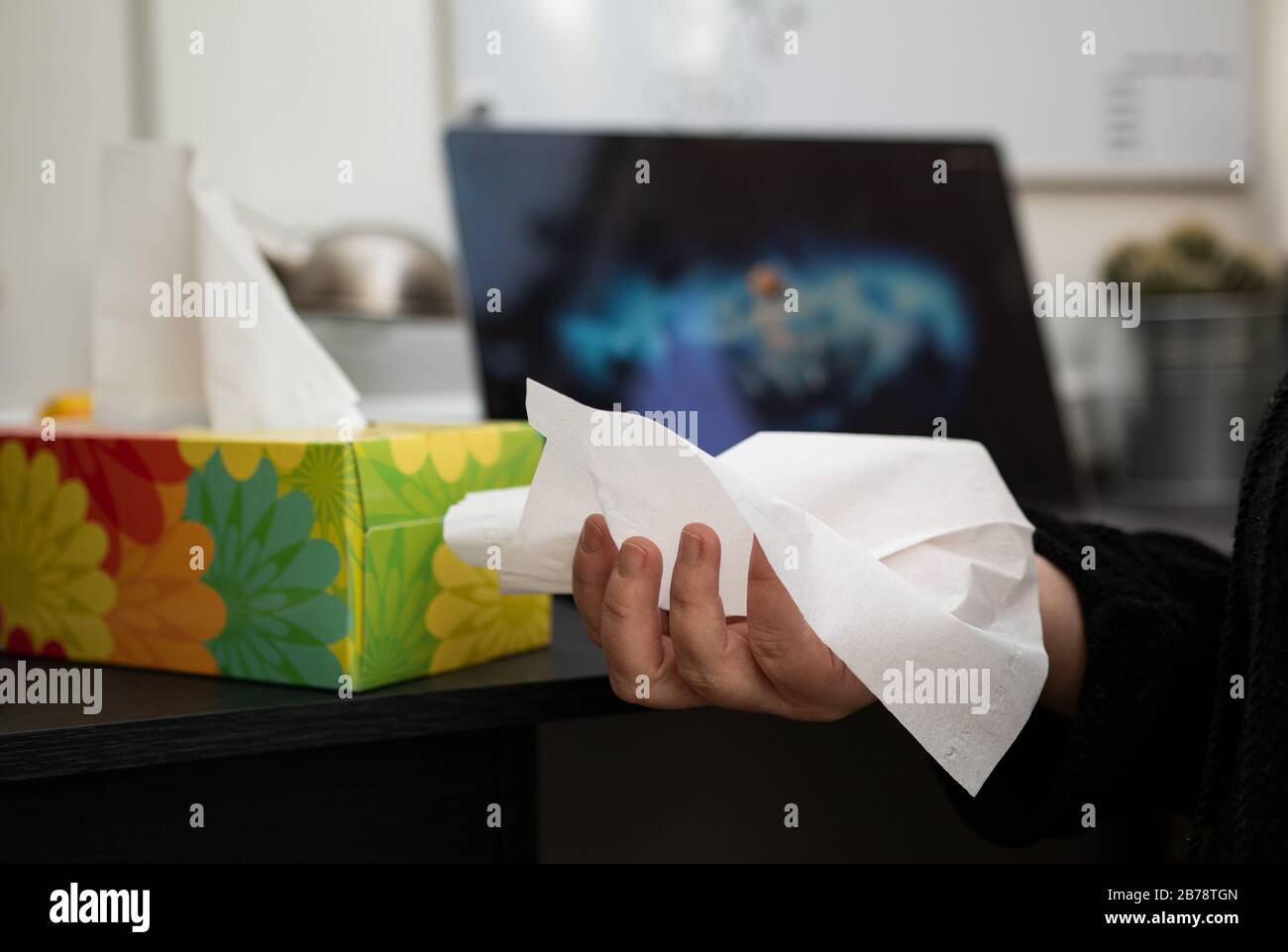 hand holding a disposable tissue, next to the tissue box in an office