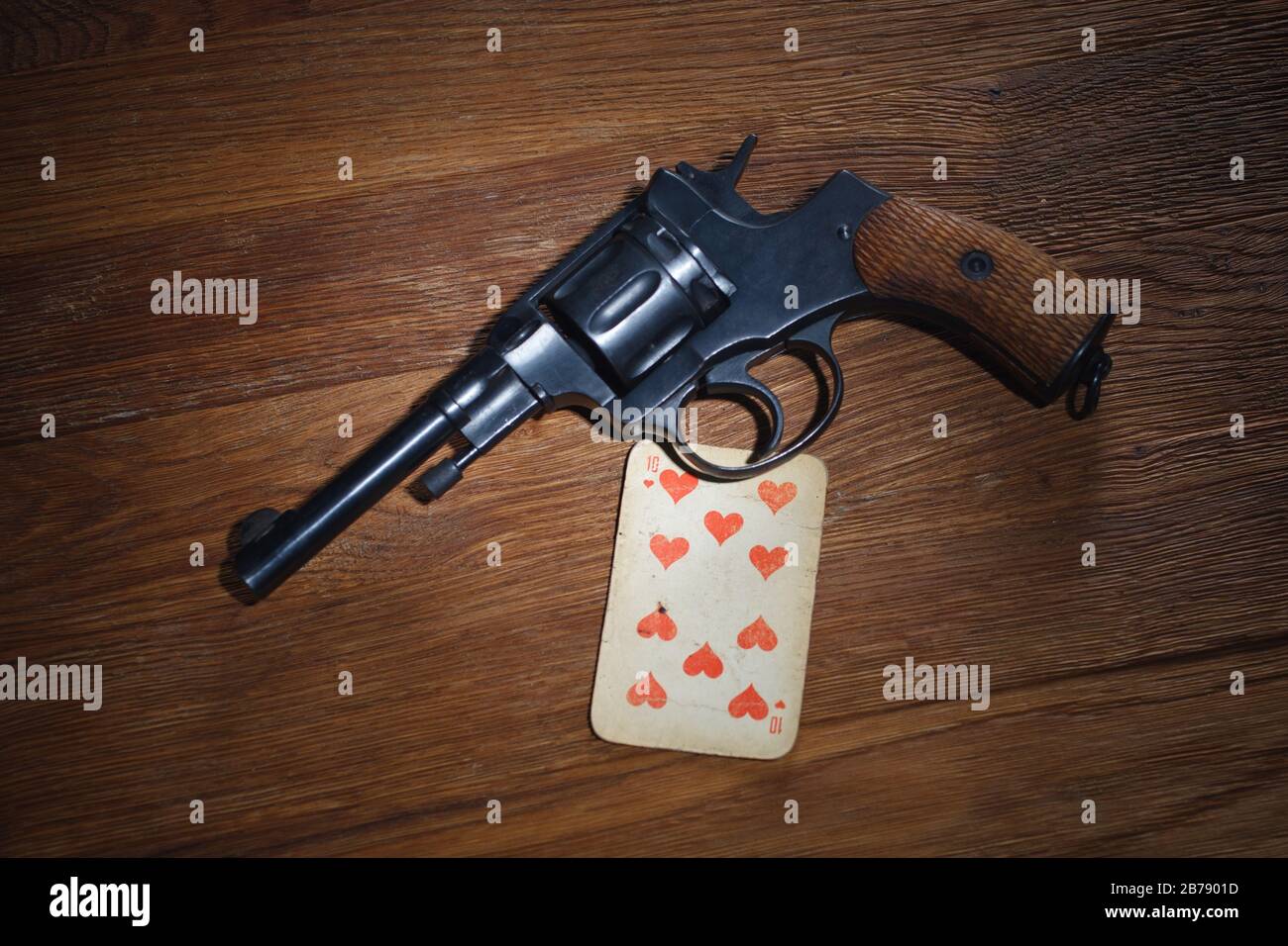 russian roulette - Ten of Hearts plaing card and revolver with one cartridge in drum on wooden table background Stock Photo