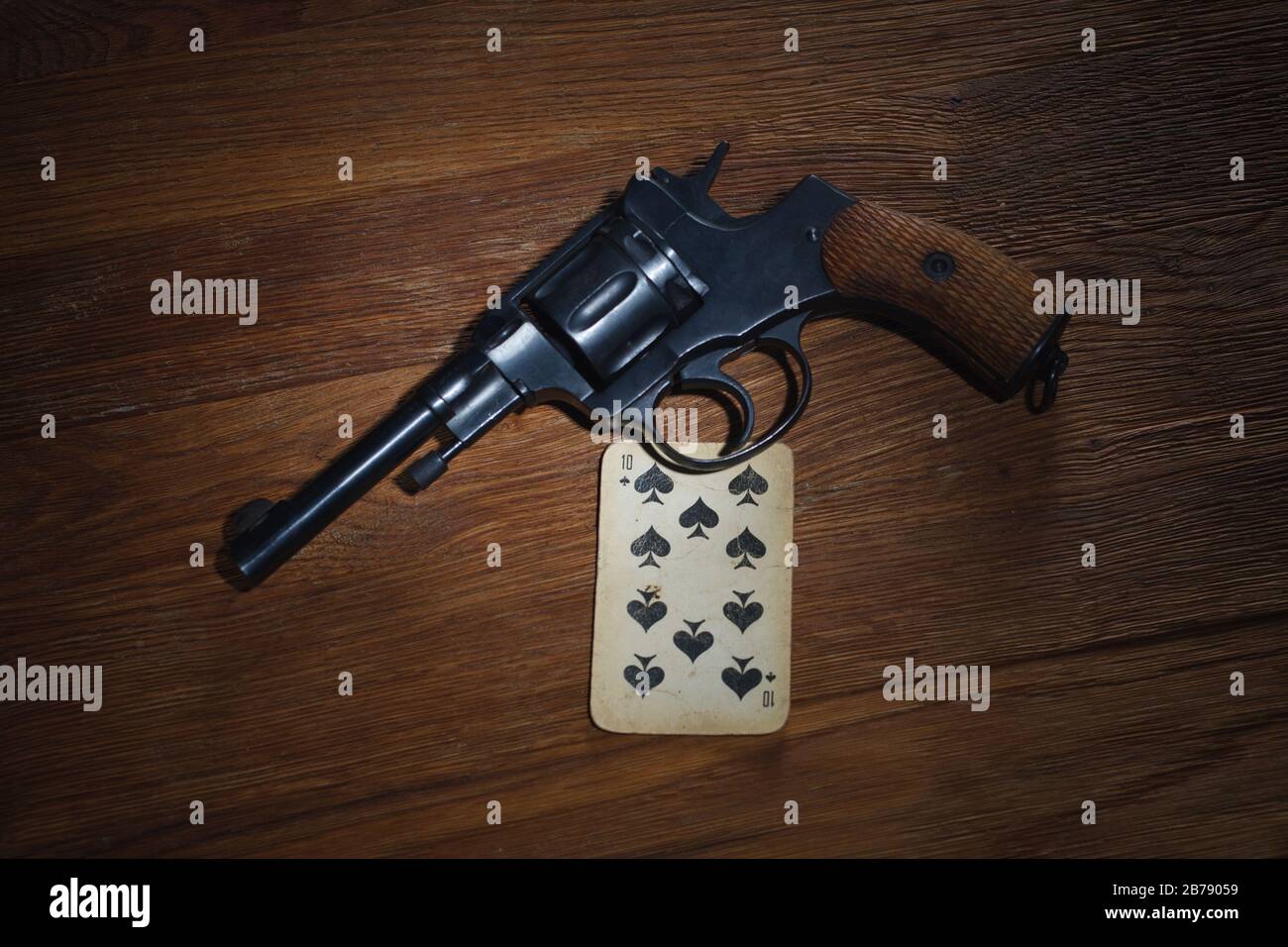 russian roulette - Ten of Spades plaing card and revolver with one cartridge in drum on wooden table background Stock Photo