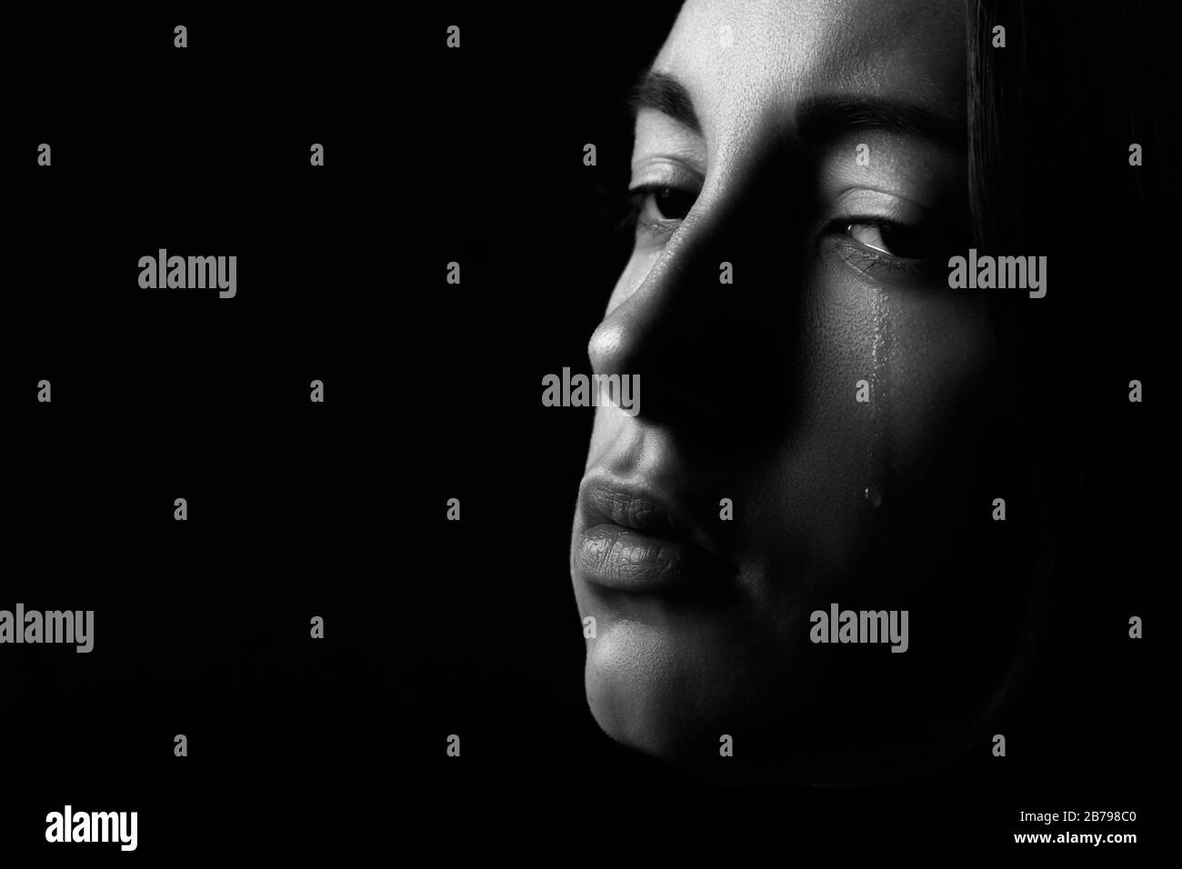 sad woman crying on black background with copy space, closeup portrait, monochrome Stock Photo