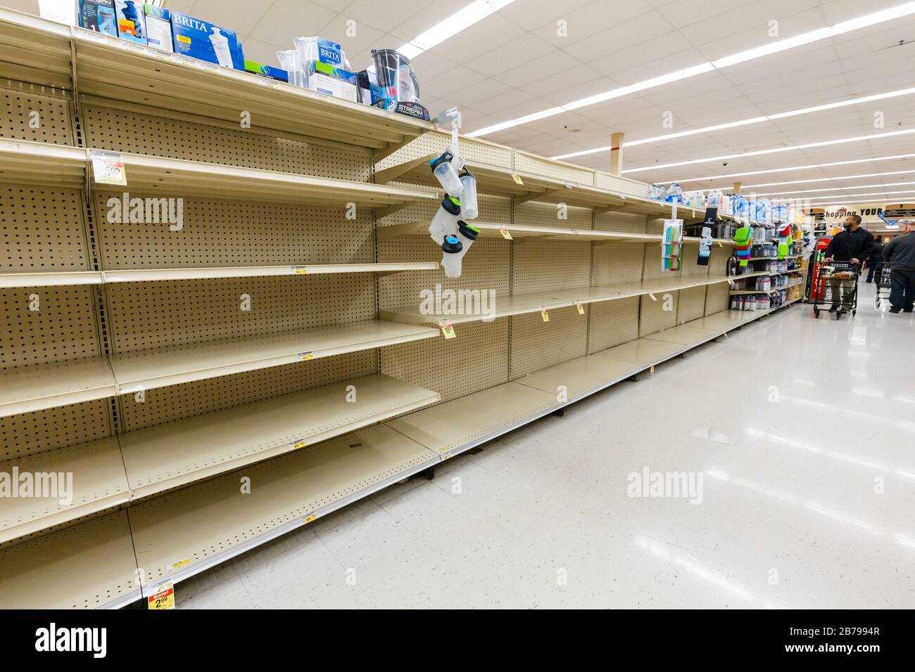 Shoppers searching for bottled water, but find empty shelves in a supermarket grocery store as coronavirus causes fear and panic horizontal Stock Photo