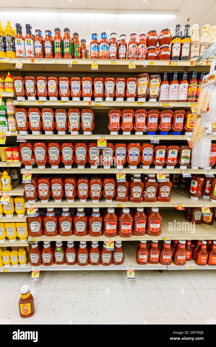 Heinz and other brands of red tomato ketchup sauce bottles fully stocked on shelves of the condiments aisle in supermarket grocery store vertical Stock Photo