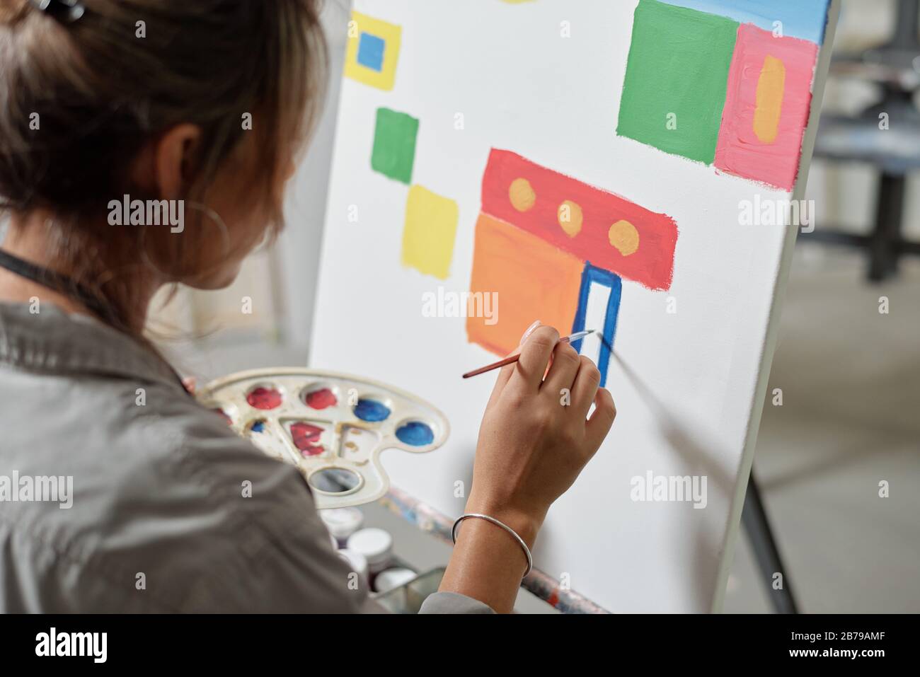 Hand of young female artist holding color palette while sitting by ...