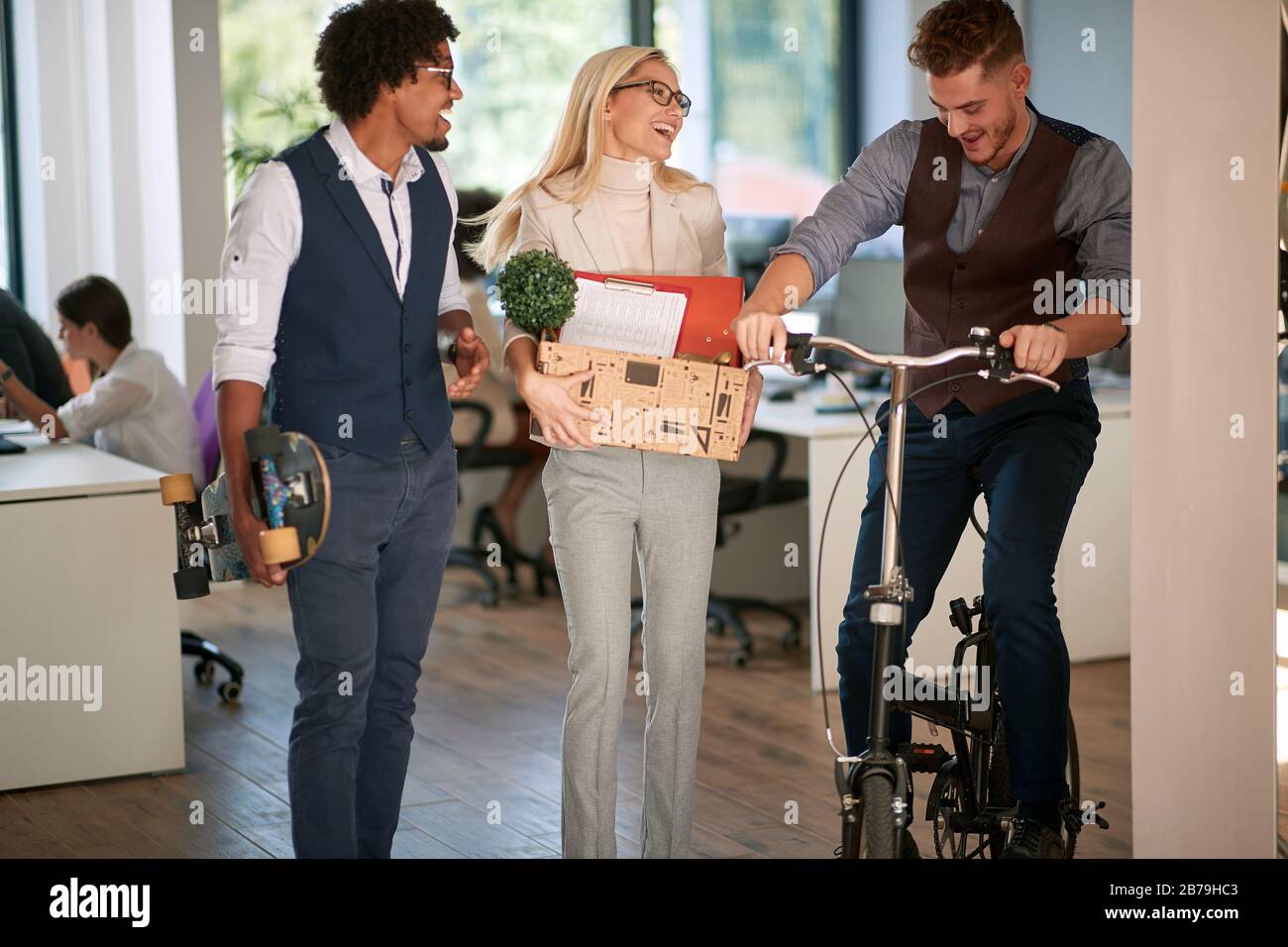 Smiling female employee with personal stuff and colleagues at office Stock Photo