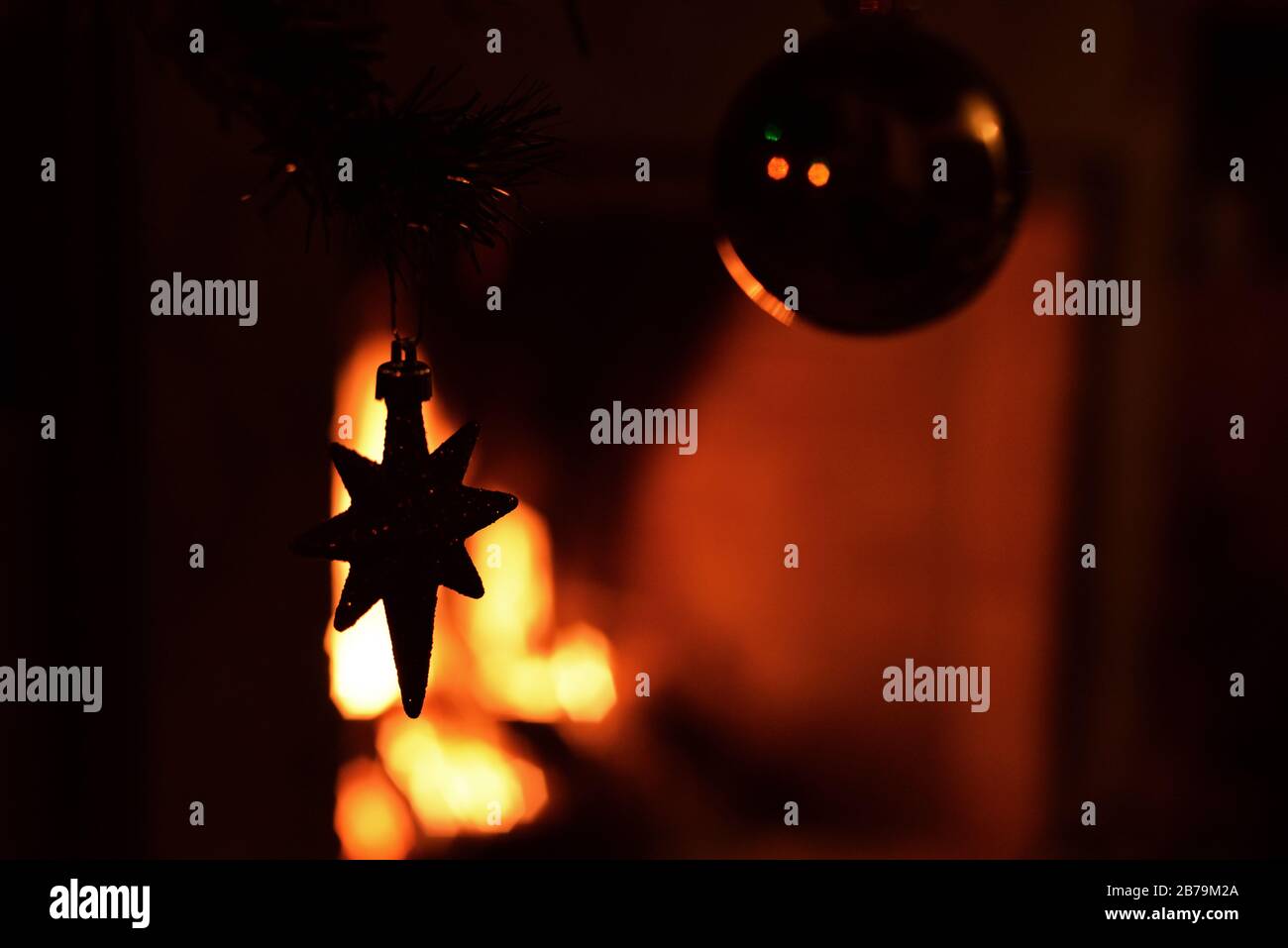 Decorative star hanging from a Christmas tree against the illumination  of a fireplace. Concept: festive season. Stock Photo