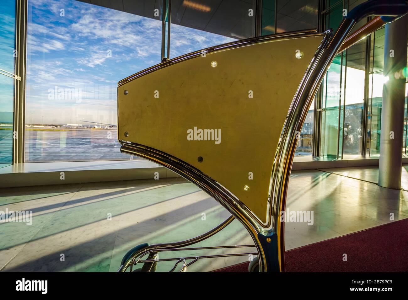 Backlighted airport luggage cart with large window panes in the background with view on the tarmac Stock Photo