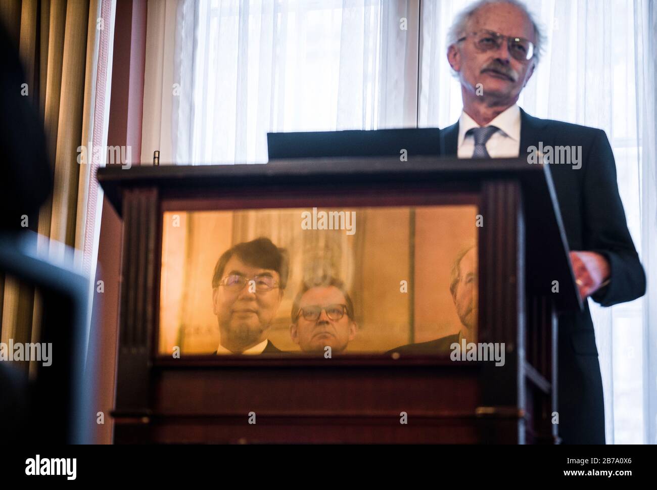 14 March 2020, Hessen, Frankfurt/Main: During the non-public presentation of the Paul Ehrlich and Ludwig Darmstaedter Prize to him, Japanese immunologist Shimon Sakaguchi (below left) is mirrored by a brass plate in the lectern, while behind him (above right) Professor Hans-Georg Rammensee from Tübingen gives the laudatory speech. The award for basic research is endowed with 120,000 euros. Due to the corona virus, the ceremony and a press conference were cancelled. Photo: Frank Rumpenhorst/dpa Stock Photo