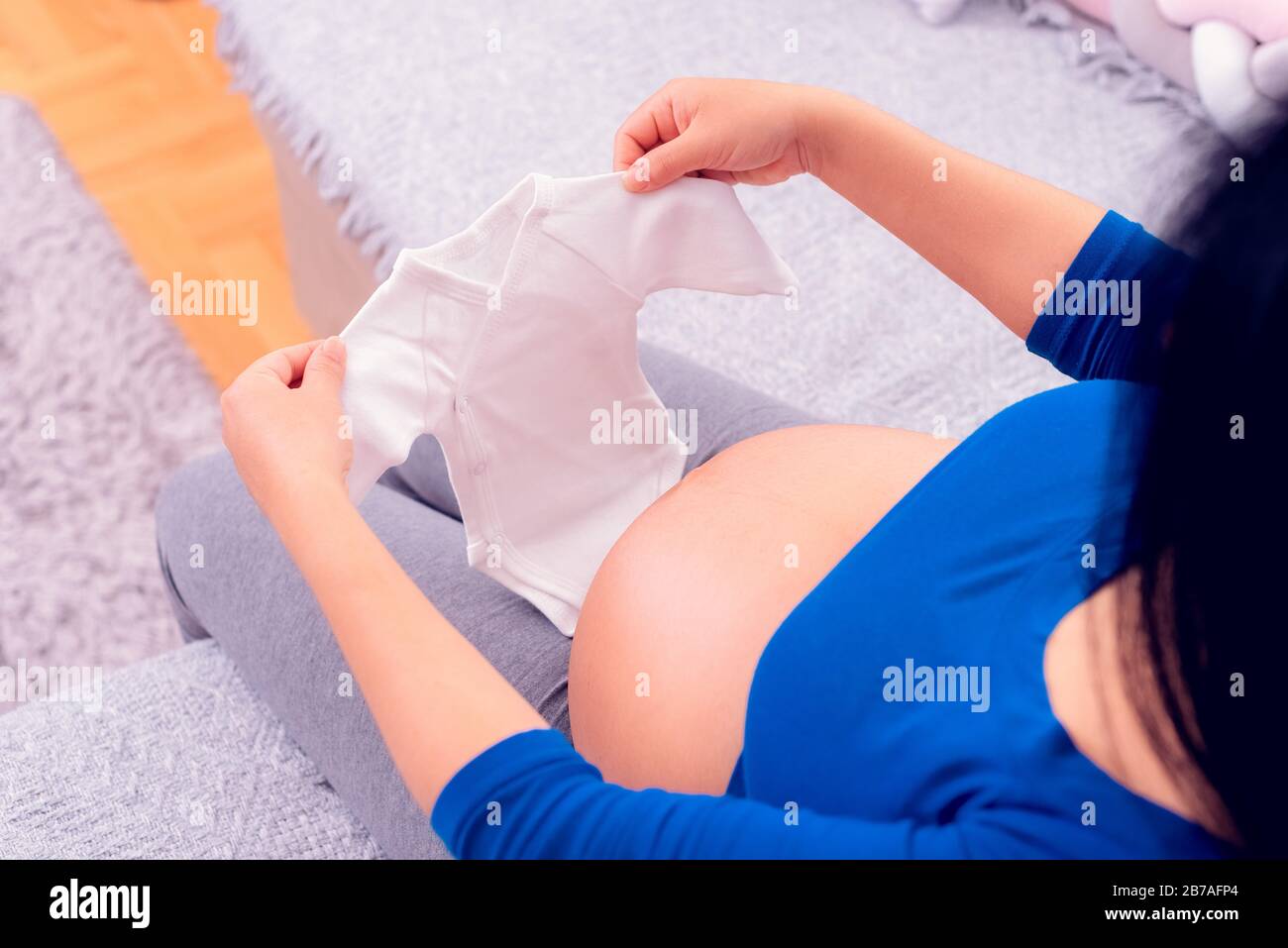 Pregnant woman holding baby body clothes on her large belly. Stock Photo
